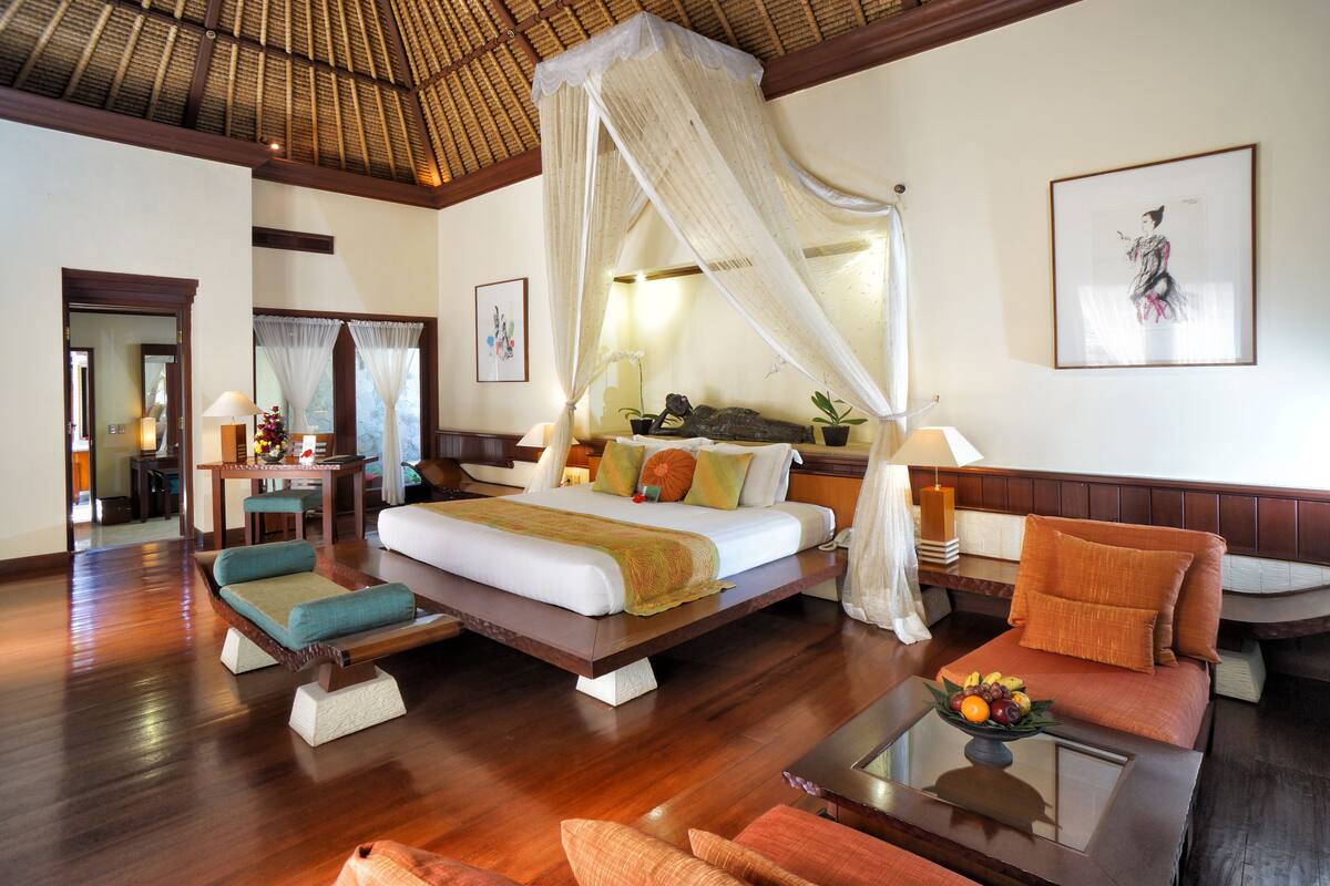 Amplia habitación de hotel con una cama grande, zona de estar con sofá y sillones, mesa de comedor y balcón con vistas.