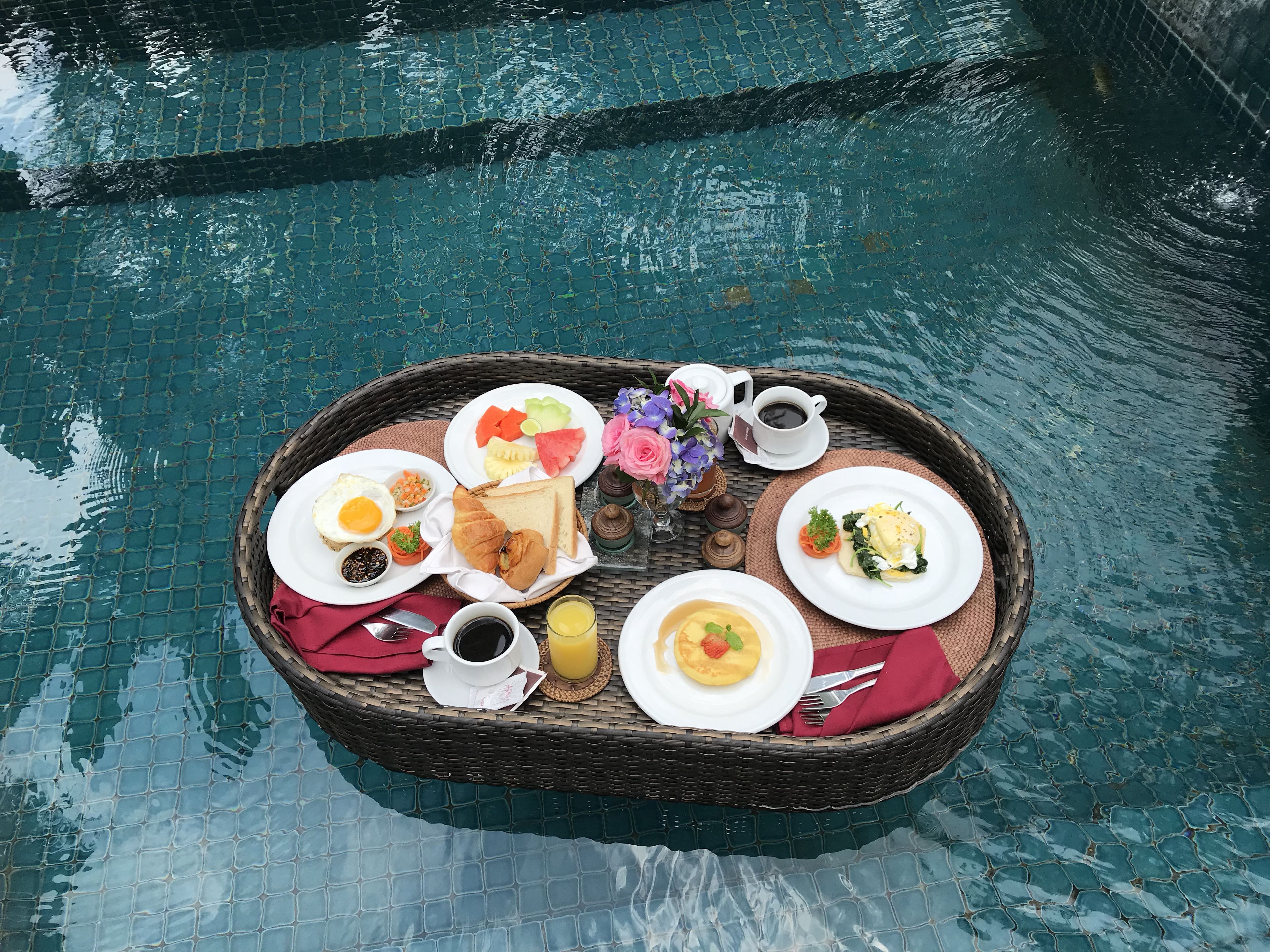 A breakfast tray with various foods and drinks by a pool.