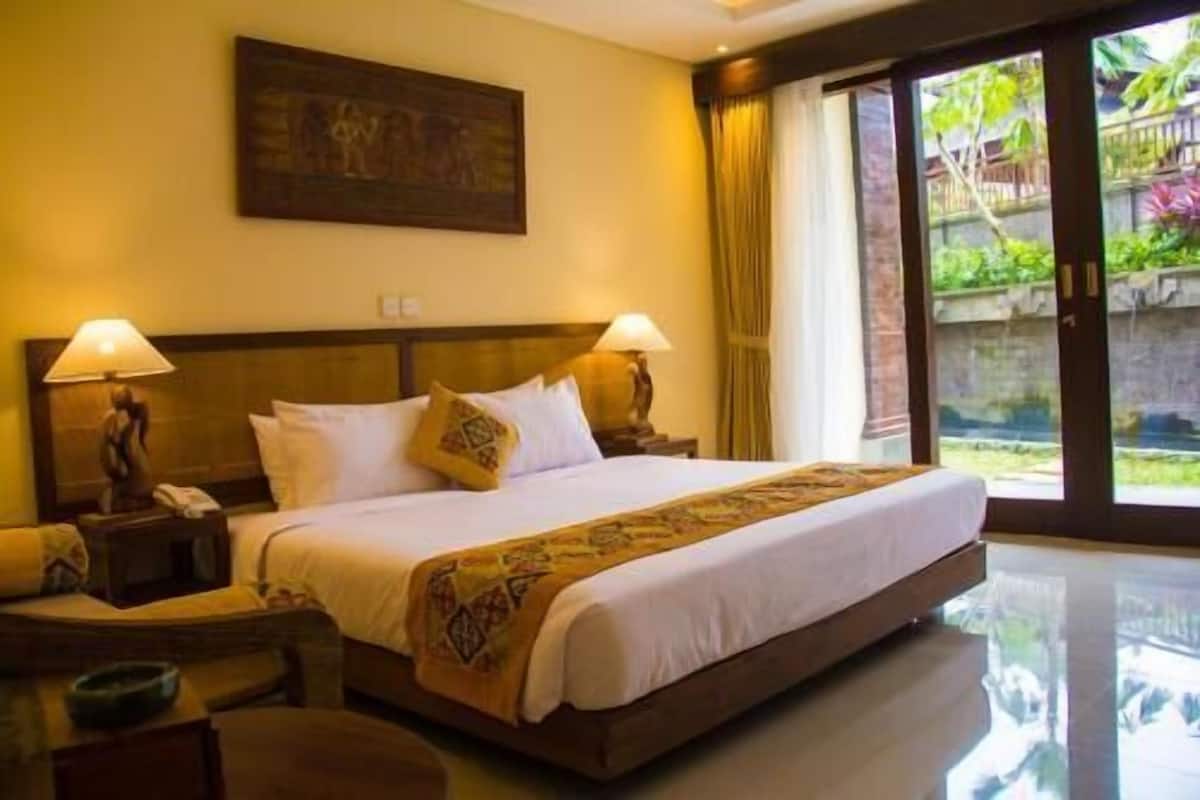 Habitación de hotel con una cama grande, dos lámparas de noche, una mesita de noche, un teléfono y un cuadro en la pared.