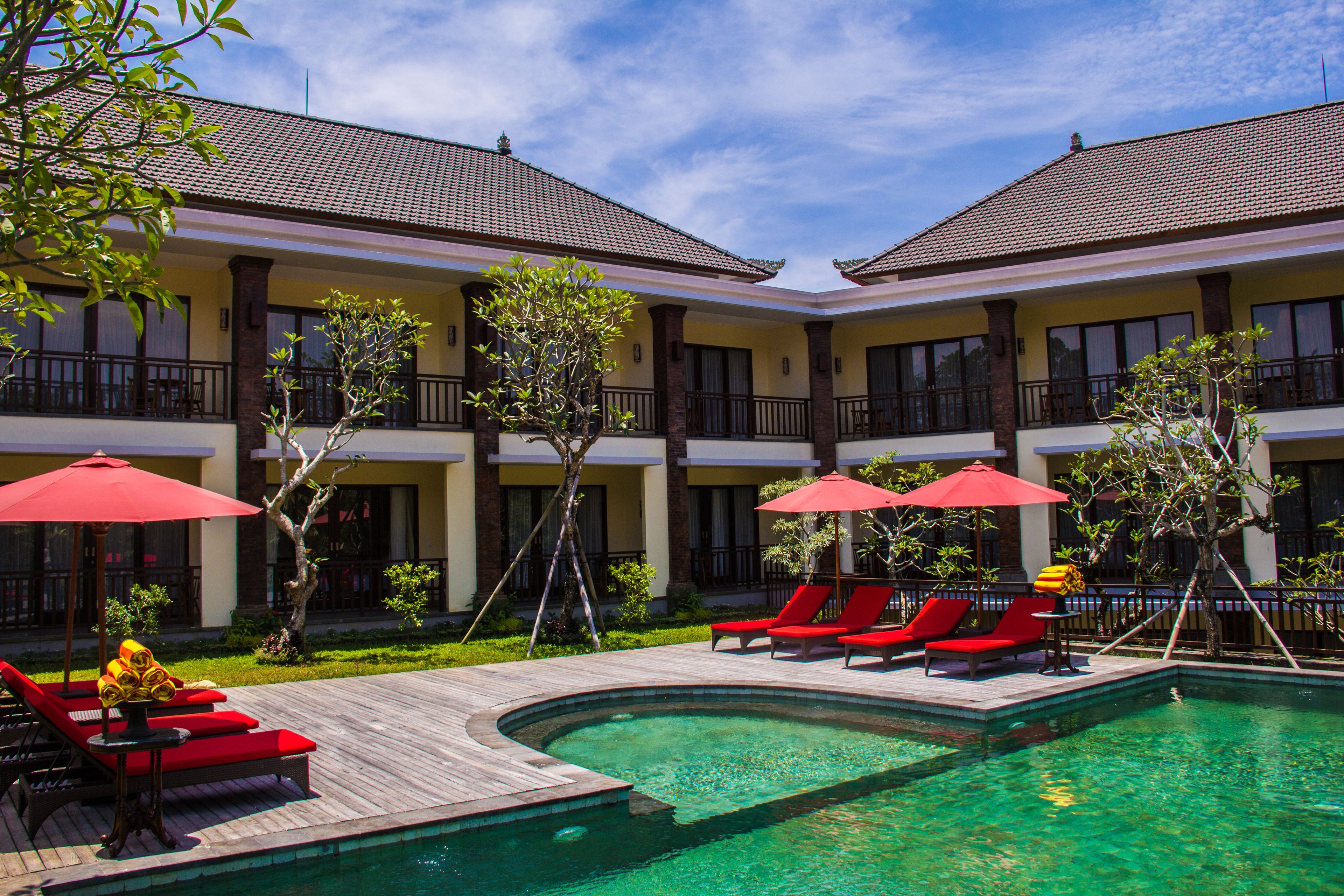 Un hôtel doté d’une piscine, de chaises longues rouges et de parasols.