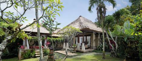 A tropical resort with thatched-roof structures, lush greenery, and a stone pathway.