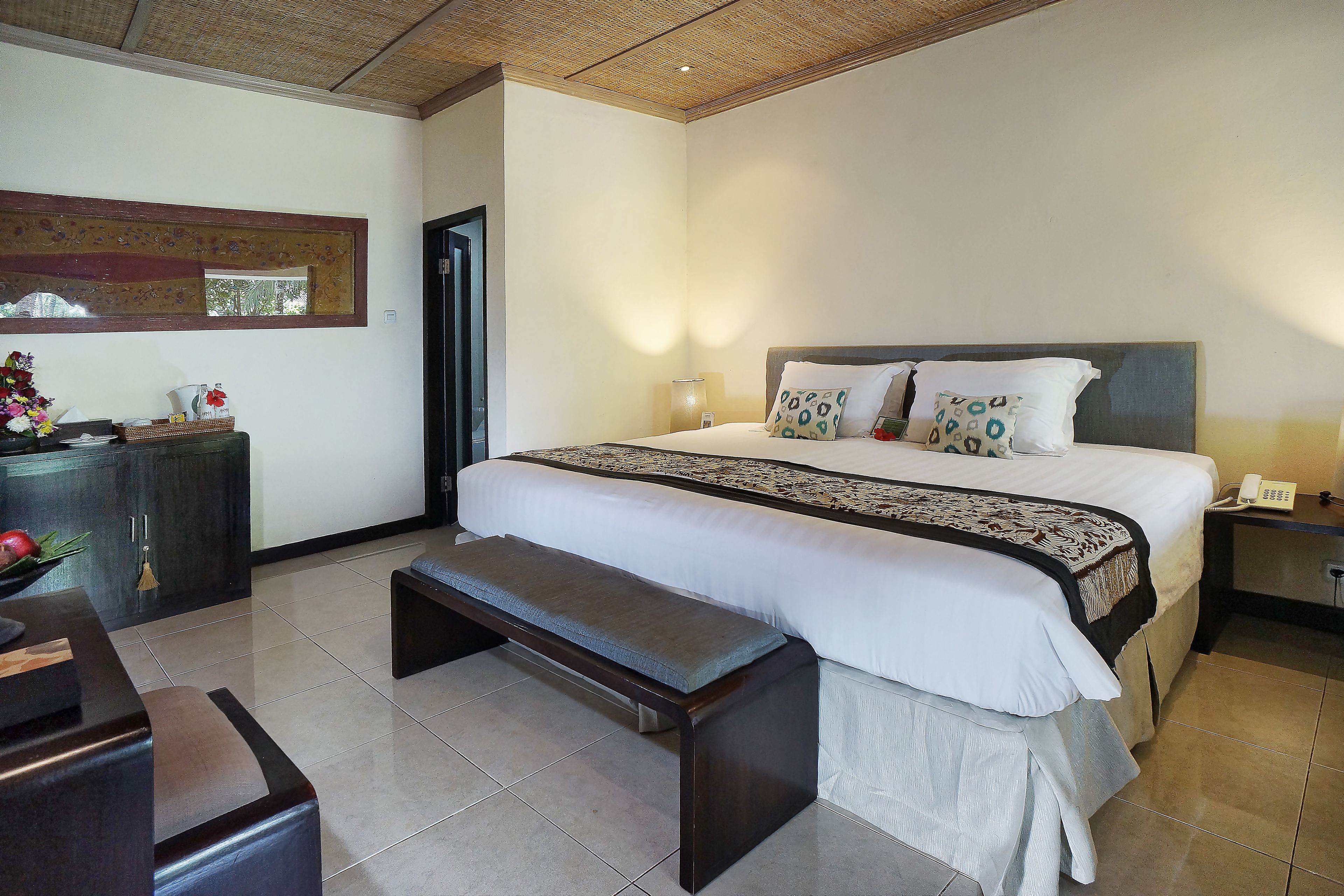 A bedroom with a bed, bedside table, bench, and a decorative mirror.