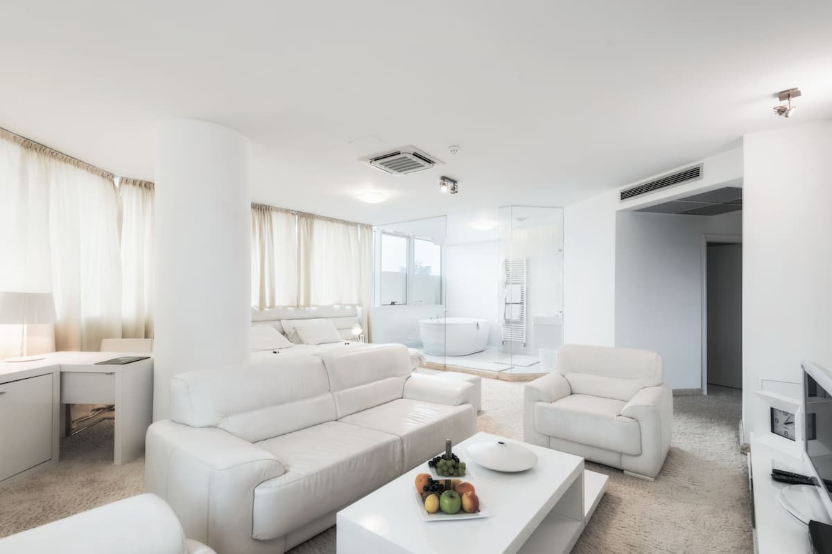 A modern, white-themed living room with a sofa, coffee table, and a TV stand.