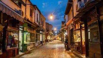 Uma rua estreita com lojas em ambos os lados, pavimentada com lajes de pedra e iluminada por postes de luz.