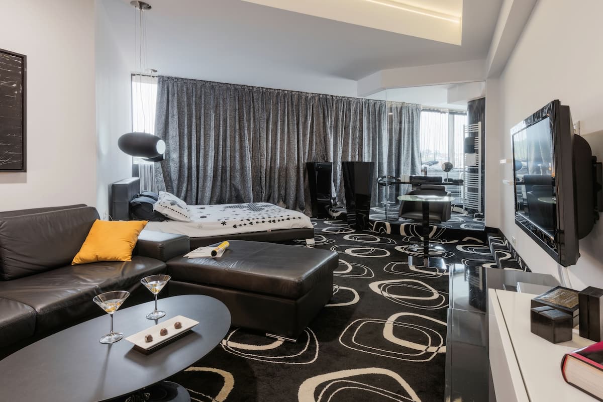 A modern hotel room with a sofa, ottoman, and a small table with a tray of chocolates.