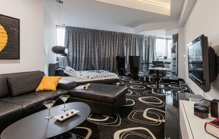Una habitación de hotel moderna con un sofá, un reposapiés y una mesita con una bandeja de bombones.
