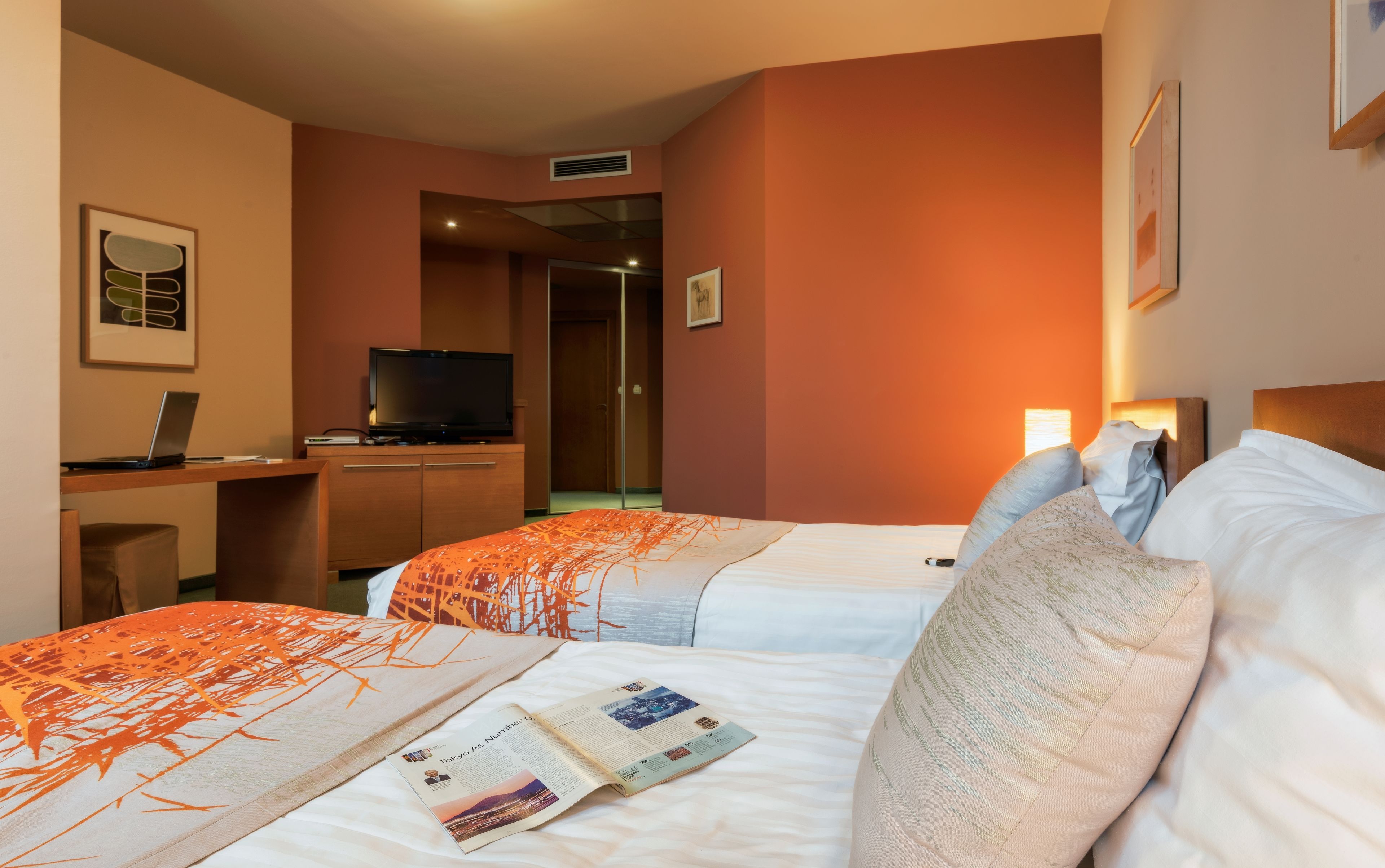 A hotel room with two beds, a desk with a laptop, a television, and a framed picture on the wall.