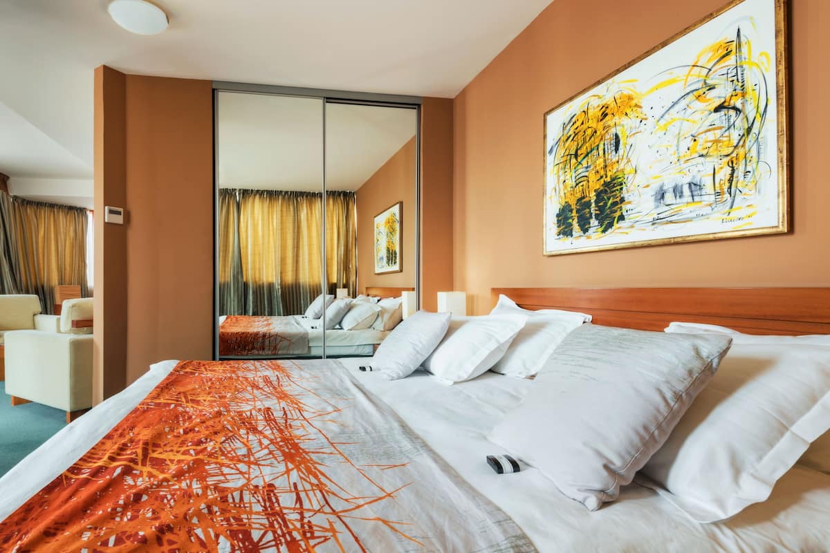 A hotel room with a large bed, a seating area with chairs, a large mirror, and artwork on the walls.