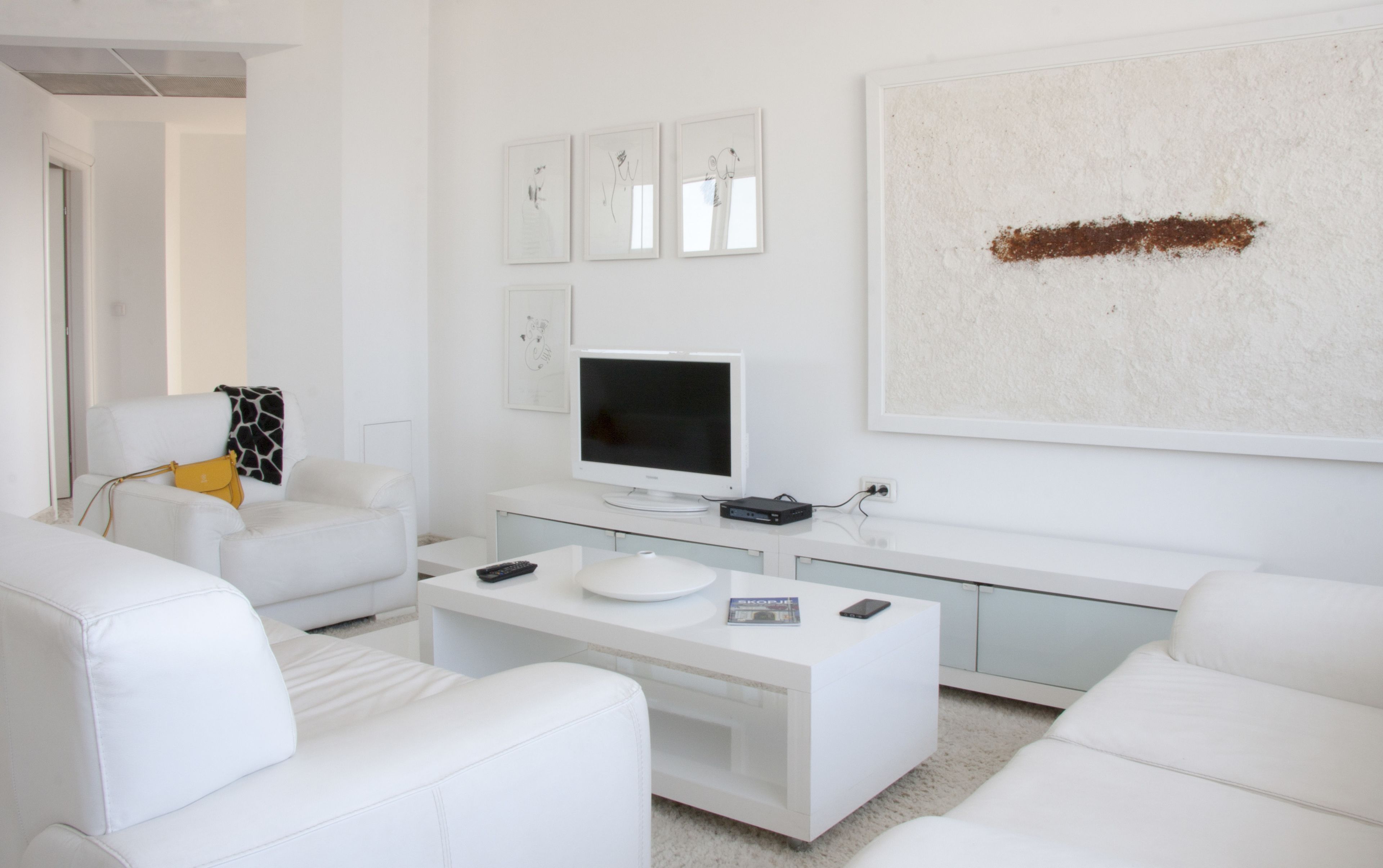Un salon moderne avec des meubles blancs, un téléviseur à écran plat et des œuvres d’art accrochées au mur.