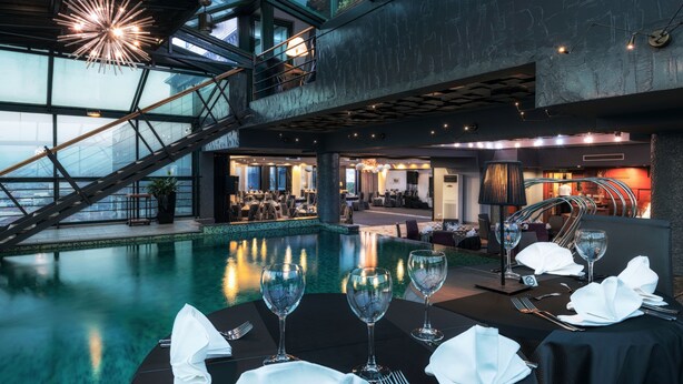 A luxurious indoor pool area with a dining setup, a staircase, and modern lighting. - Hotel Arka (Skopje)
