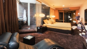 A modern hotel room with a large bed, a sitting area with a chair and a small table, a bathroom with a sink and a mirror, and a large window with curtains. - Hotel Arka (Skopje)