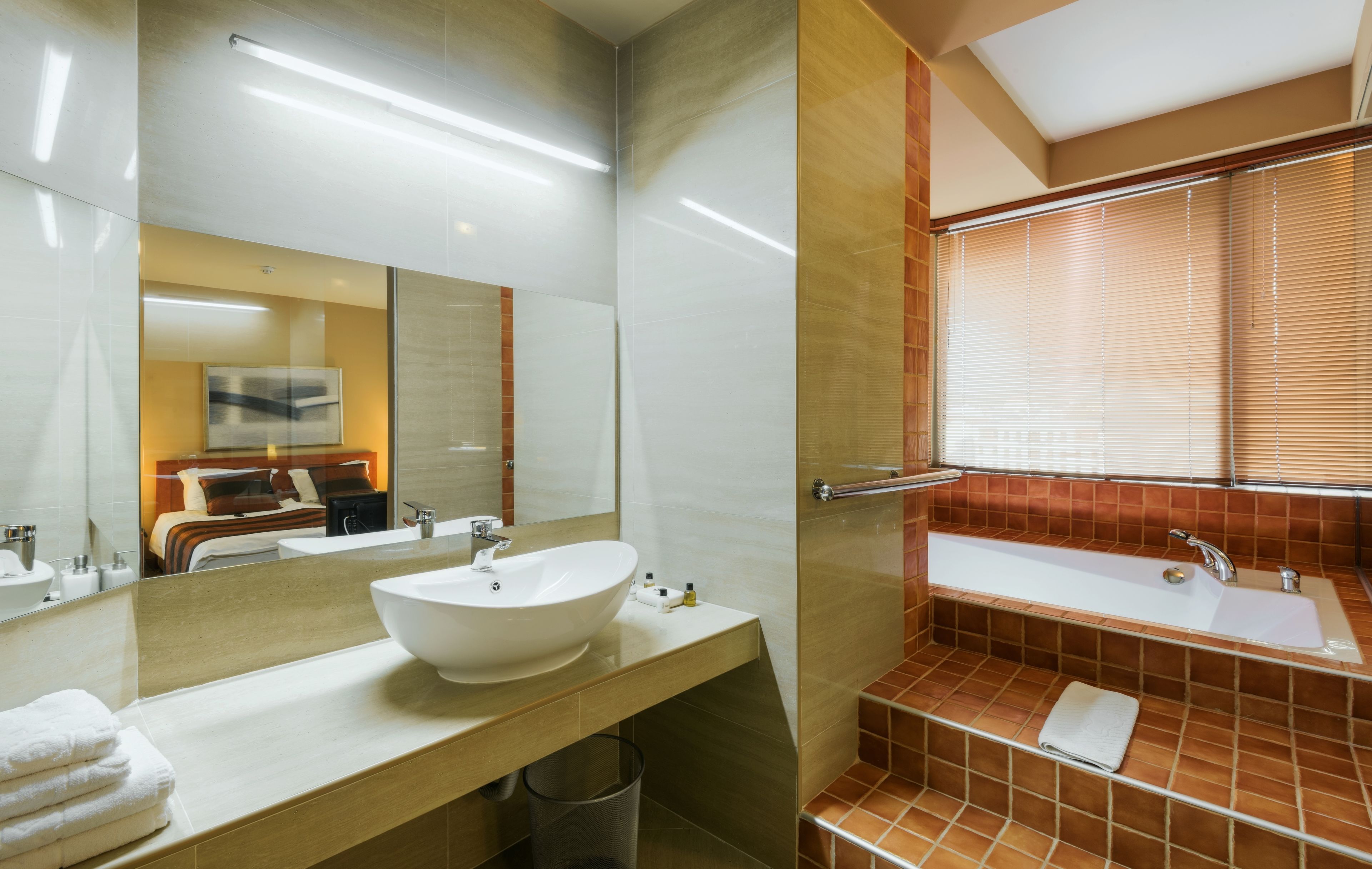 A modern bathroom with a large mirror, a white sink, and a bathtub.