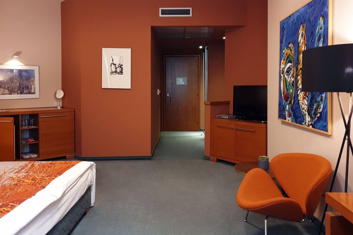 A hotel room with a bed, a desk, a chair, a television, and artwork on the walls.