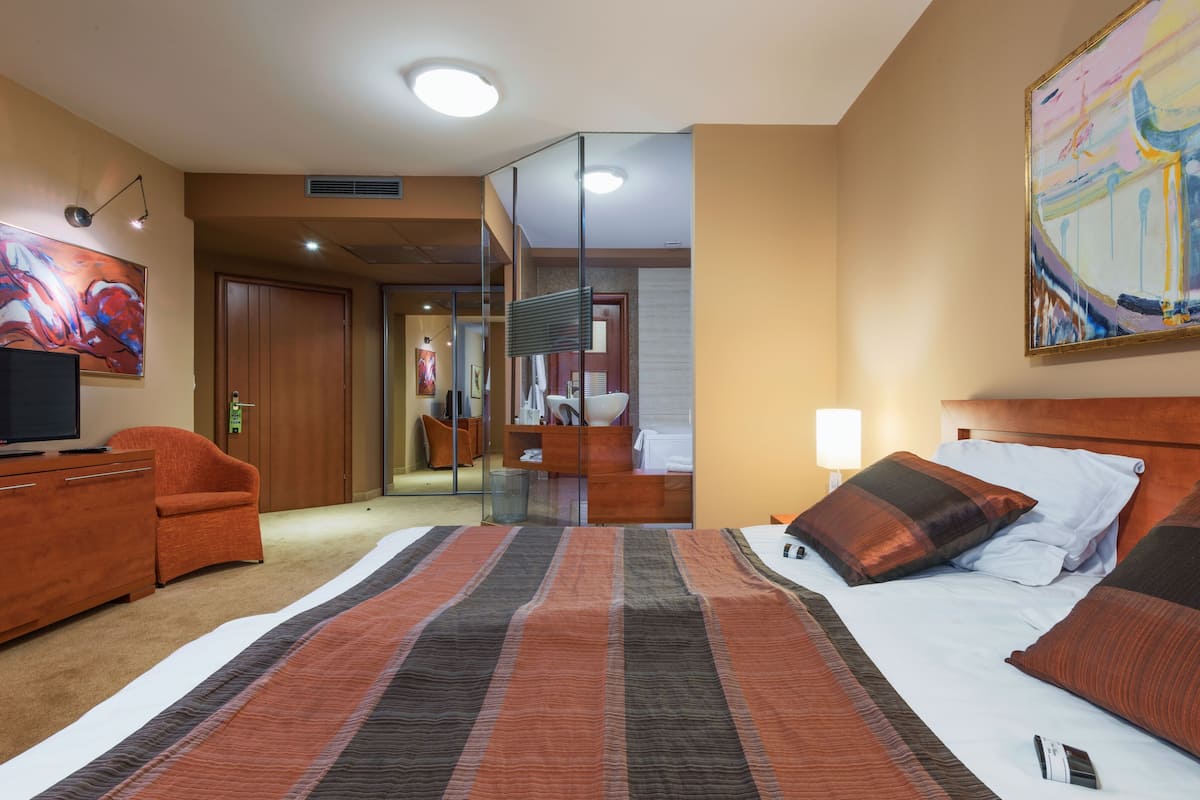 A hotel room with a bed, a desk, a chair, a TV, and a painting.