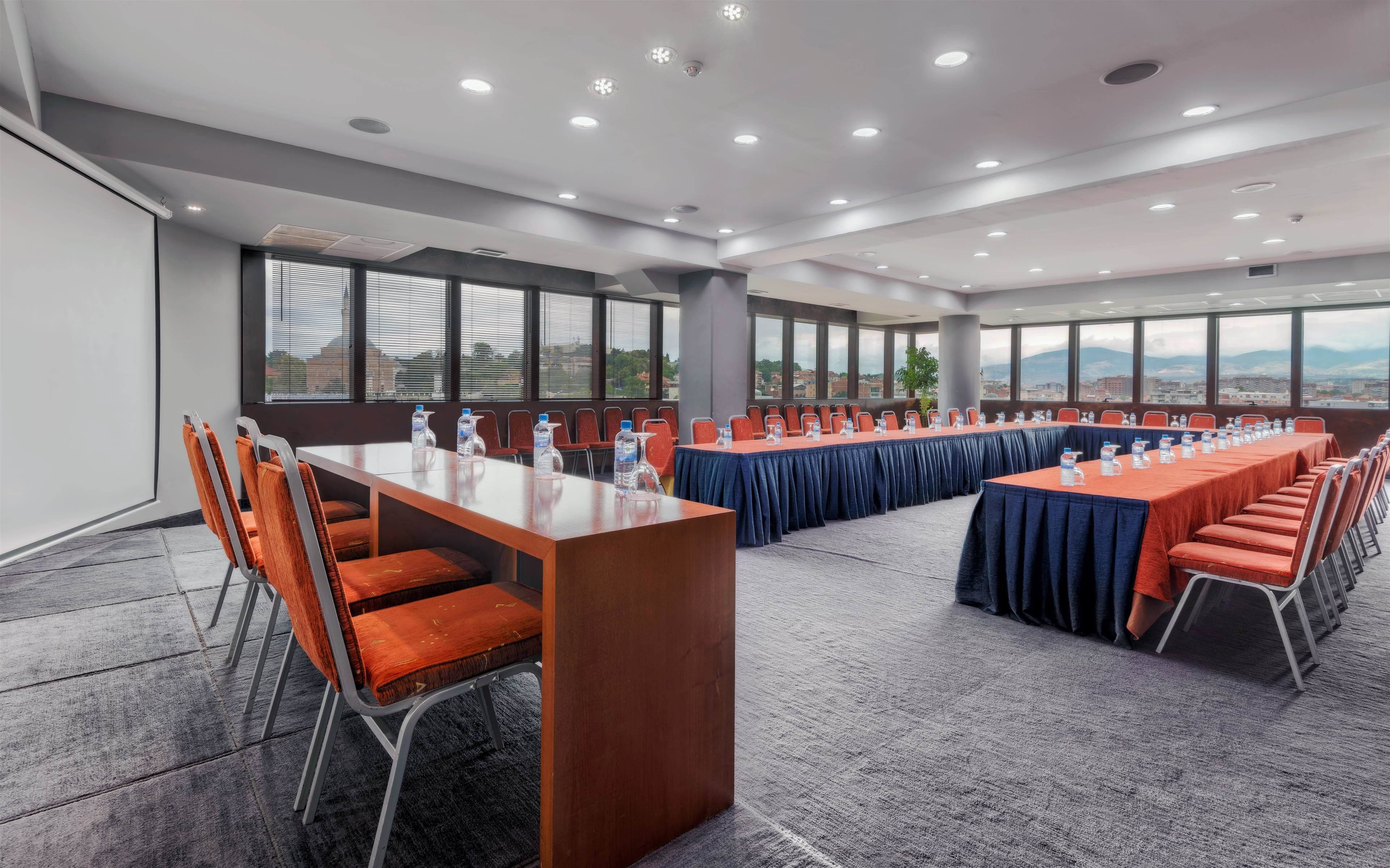 Une salle de conférence dotée de plusieurs tables et de nombreuses chaises, de grandes fenêtres et offrant une vue sur la ville.