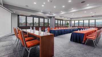 Une salle de conférence dotée de plusieurs tables et de nombreuses chaises, de grandes fenêtres et offrant une vue sur la ville.