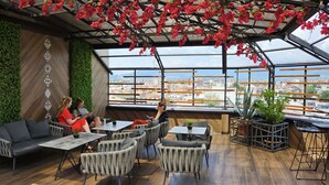 An indoor seating area with a view of a cityscape through large windows, wooden flooring, and green walls. - Hotel Arka (Skopje)