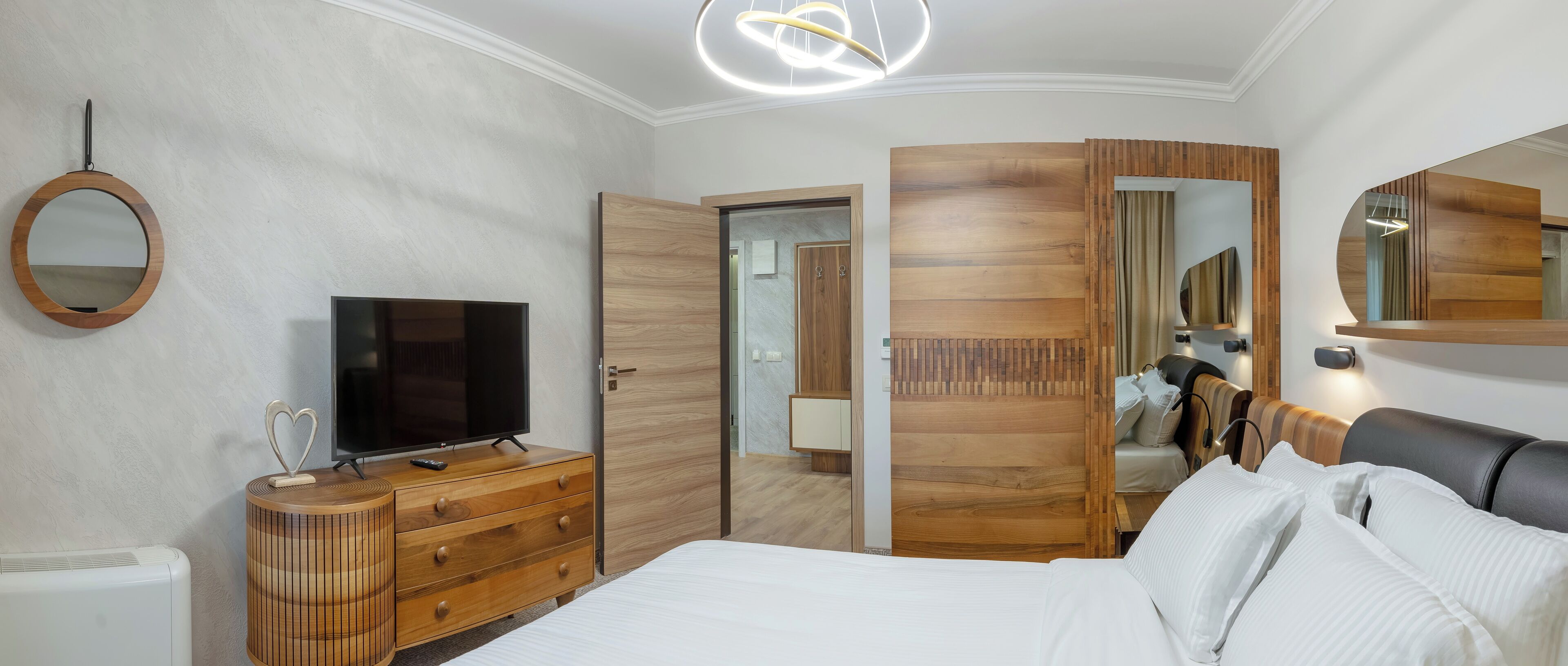 Un dormitorio con una cama, un televisor sobre un aparador de madera, un espejo y un armario de madera.