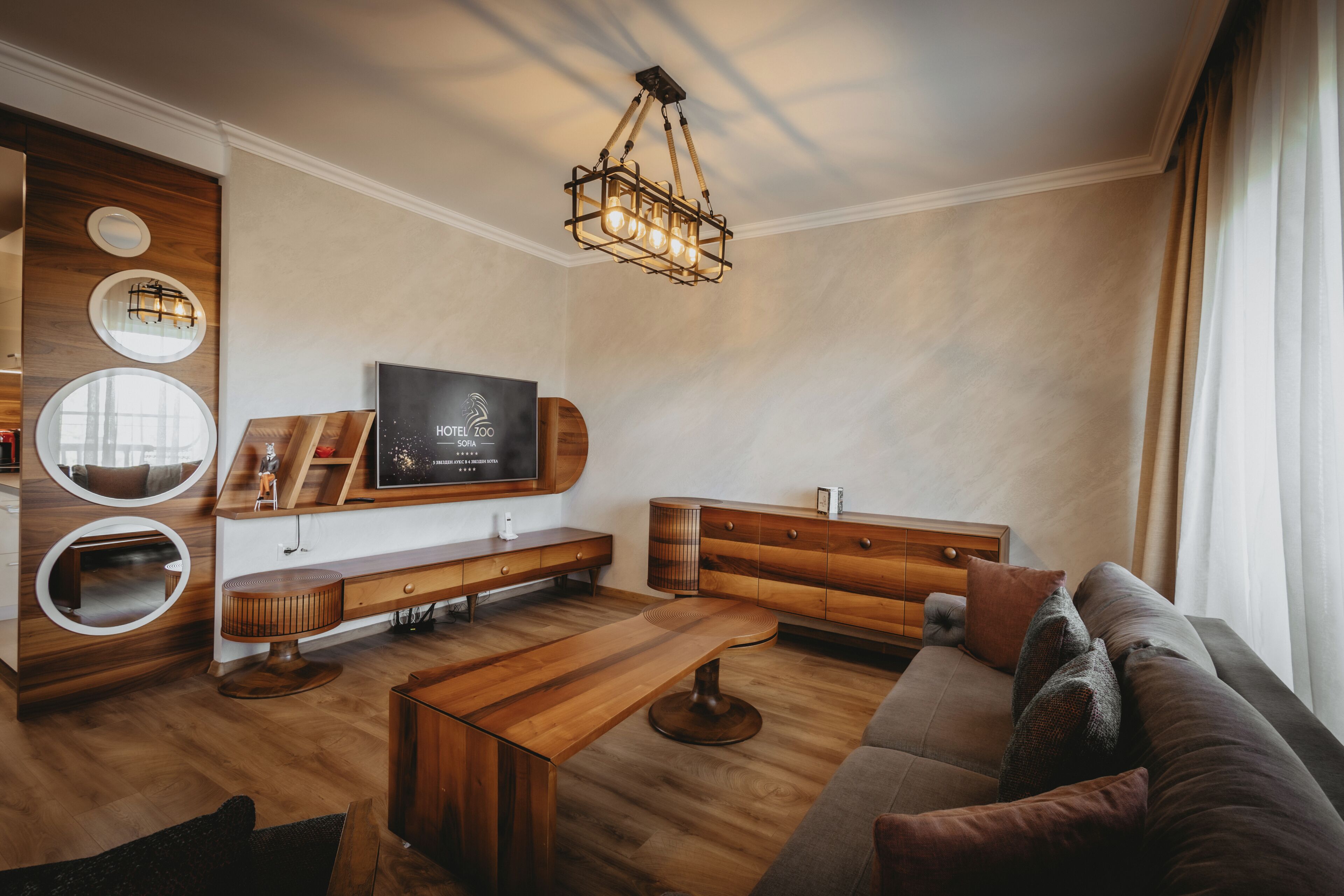 A modern living room with a wooden coffee table, a sofa, a TV mounted on the wall, and a unique circular mirror design.
