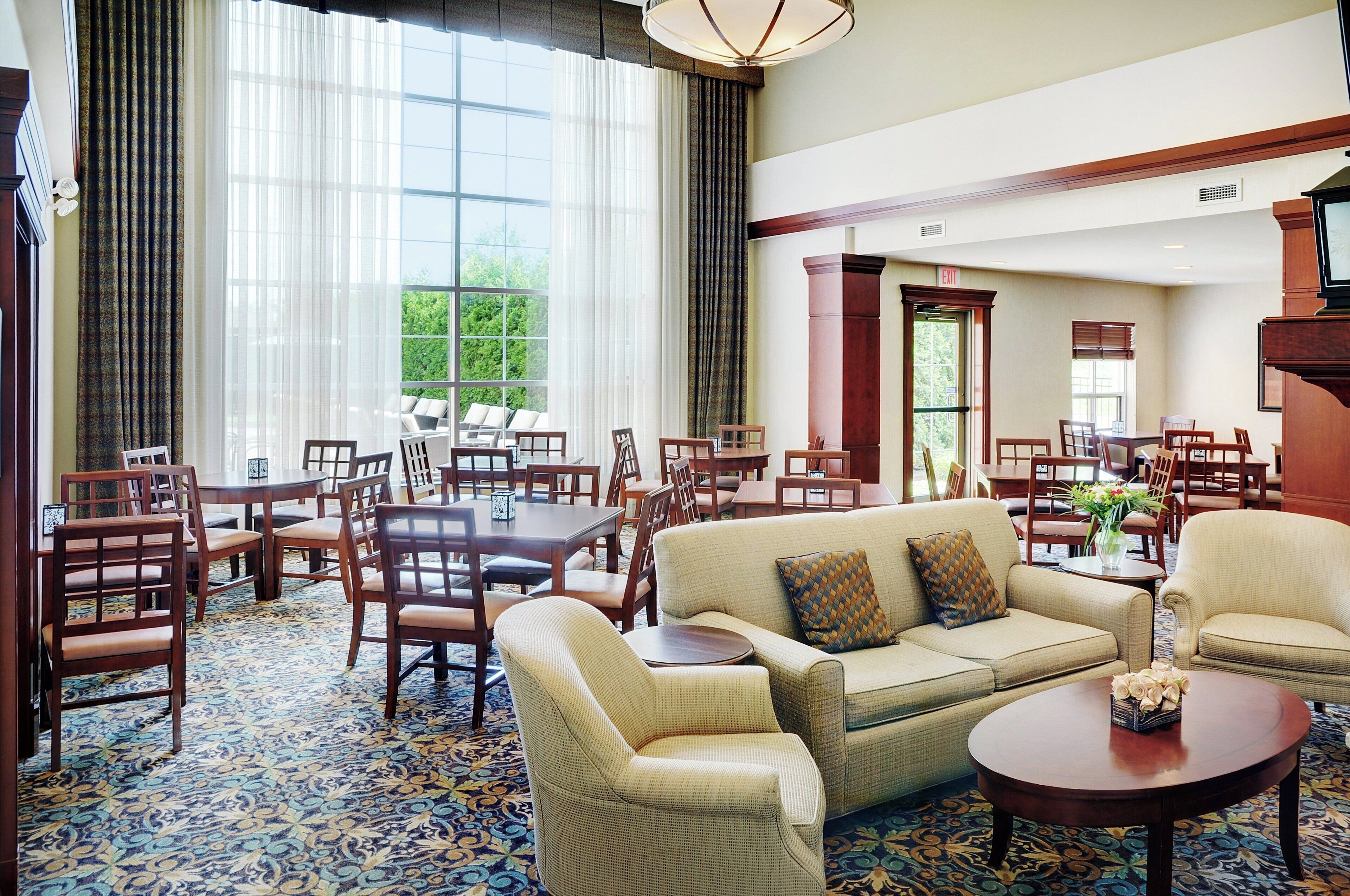 A spacious hotel lobby with a large dining area, comfortable seating, and a view of greenery outside.