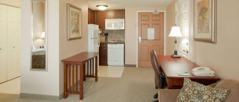 A compact hotel room with a kitchenette, a dining area with a table and chairs, and a living area with a sofa.