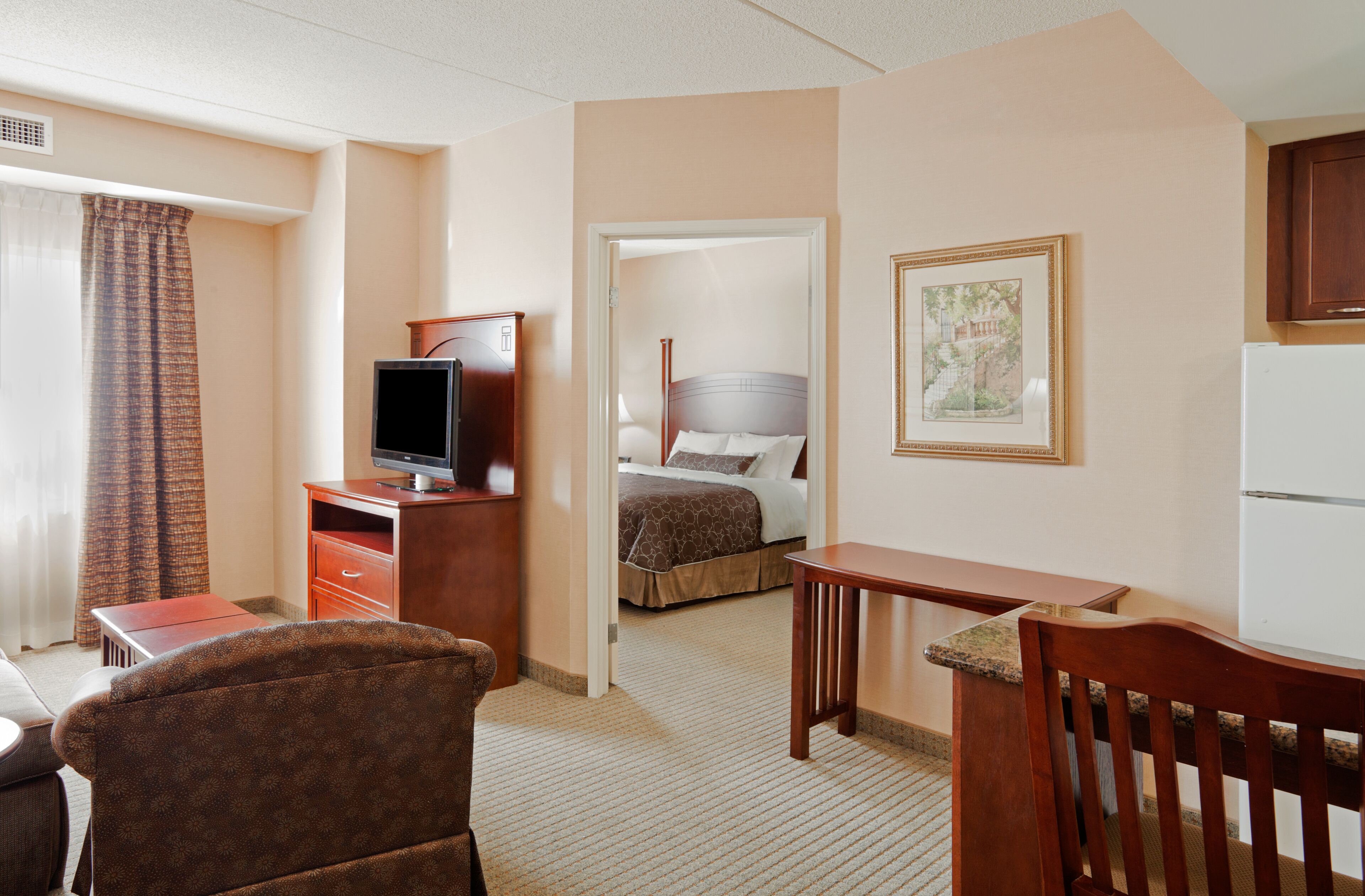 Ein Hotelzimmer mit einem Bett, einem Schreibtisch, einem Sessel, einem Fernseher und einem Kühlschrank.