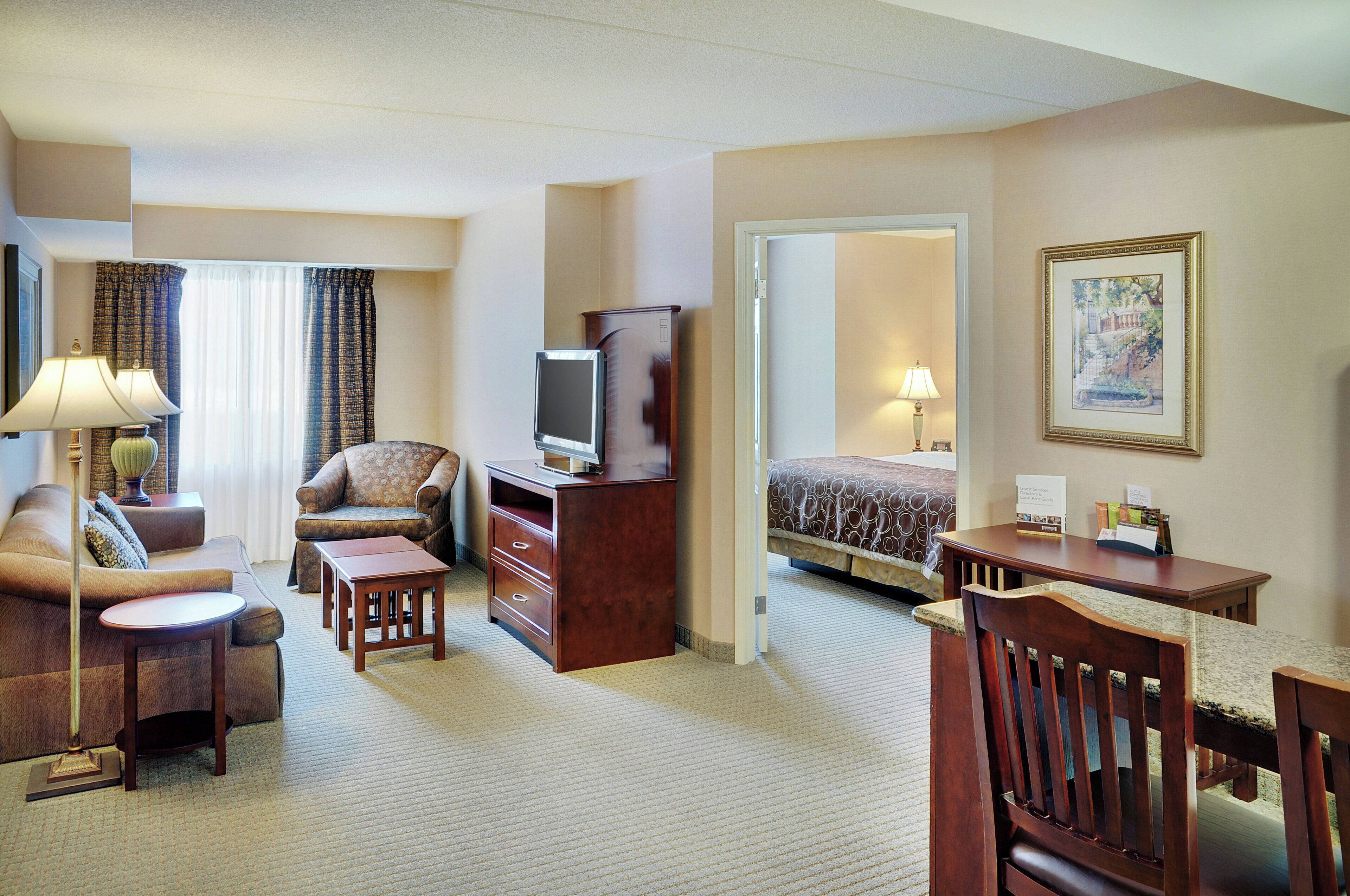 A hotel room with a sofa, a desk, a television, a dresser, and a bed.