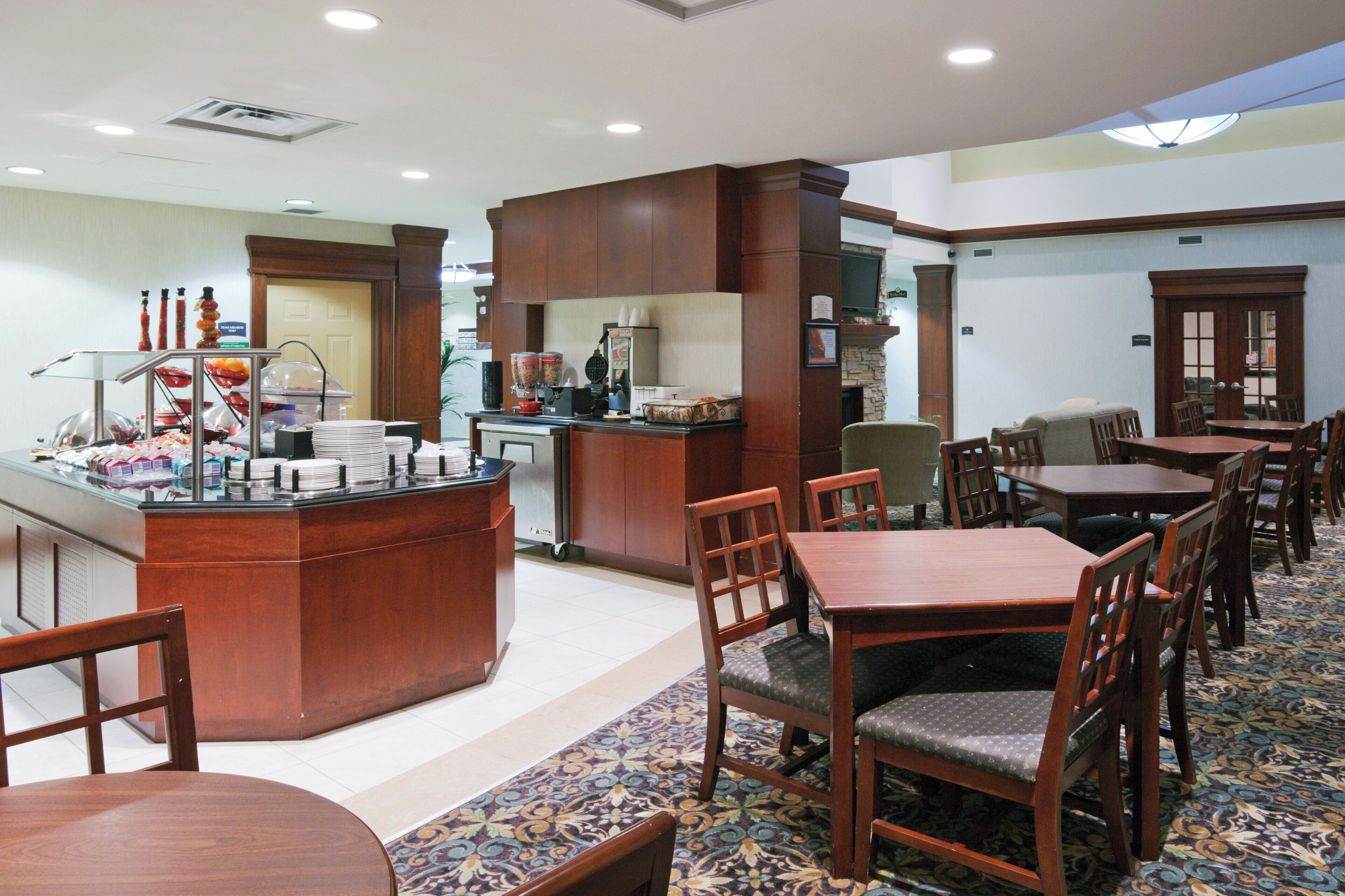 A hotel dining area with a buffet station, multiple tables and chairs, and a patterned carpet.