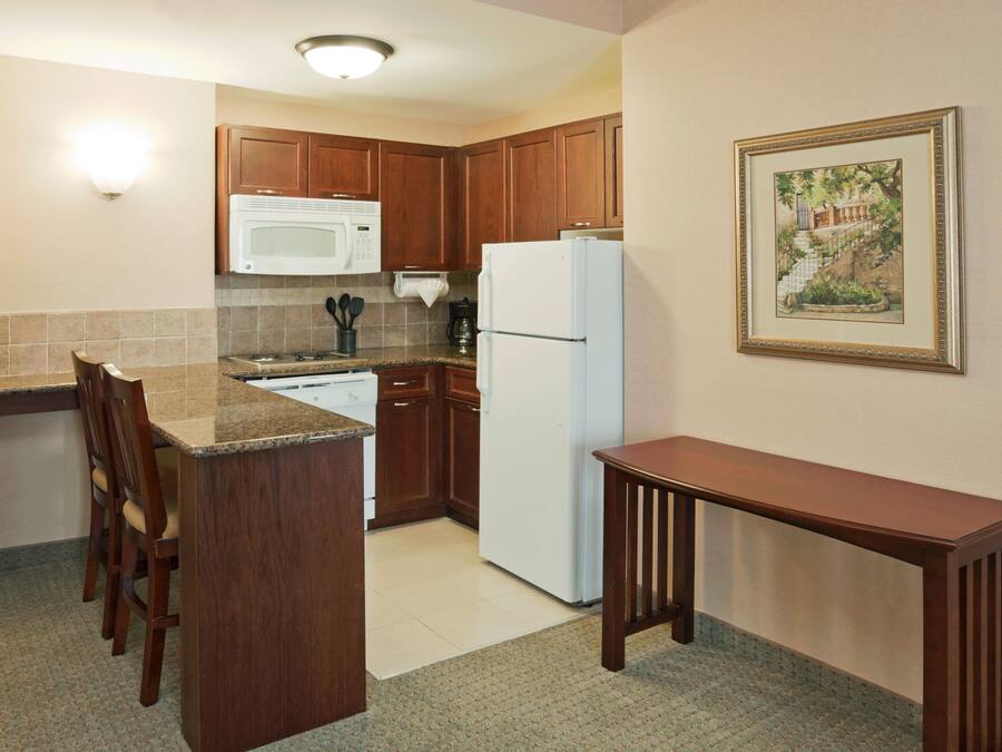 Una cocina compacta con armarios de madera, un refrigerador blanco, un microondas y una zona de comedor con una mesa y sillas.