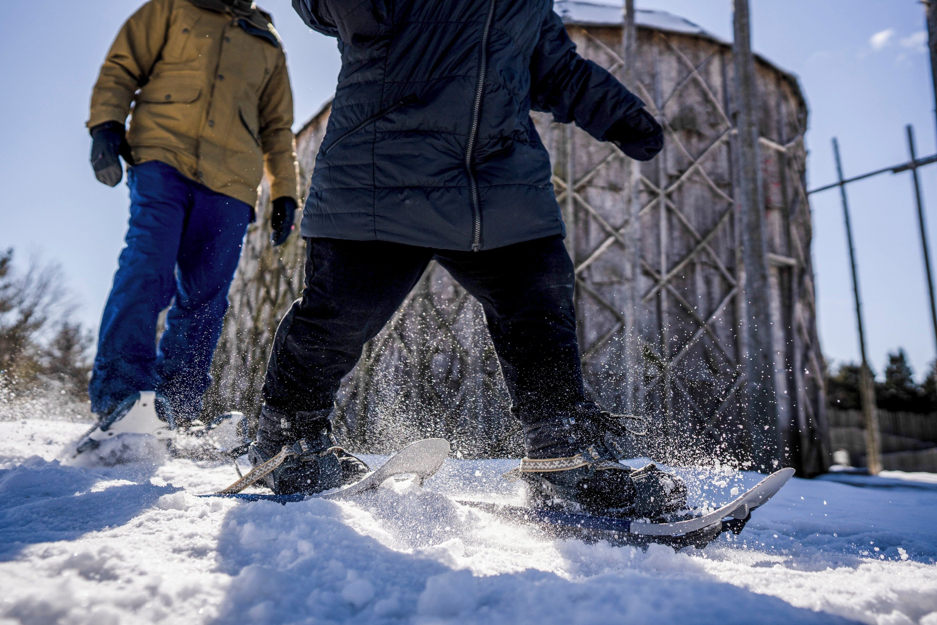Two people snowboarding on a snowy surface with a metal structure in the background.