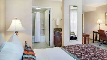 Habitación de hotel con cama, escritorio, silla, baño con ducha y espejo.