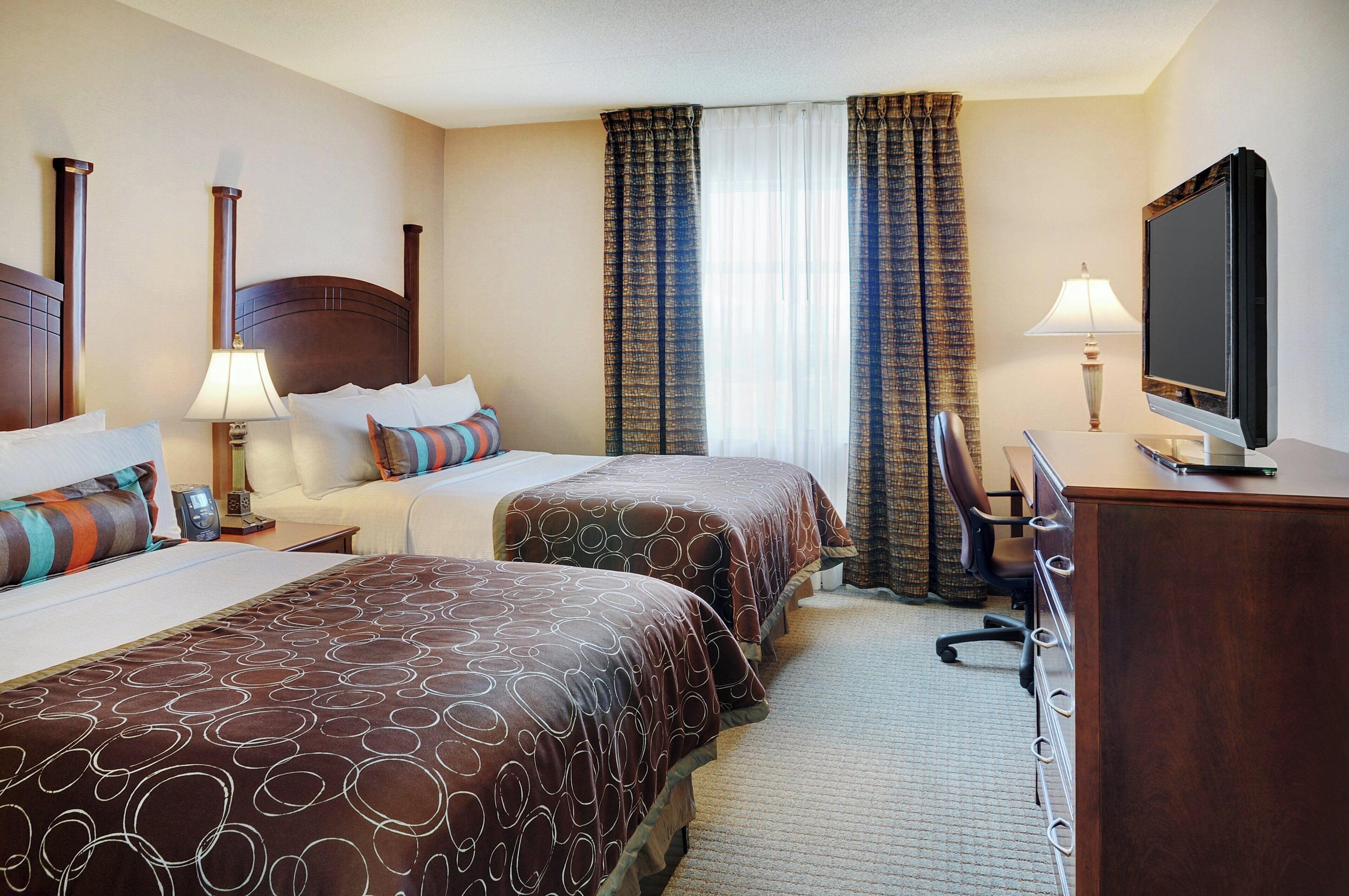 A hotel room with two beds, a desk, a chair, a television, and curtains.