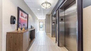 Een hal met een houten receptiebalie, omrande kunstwerken, een plafondlamp en een lift.