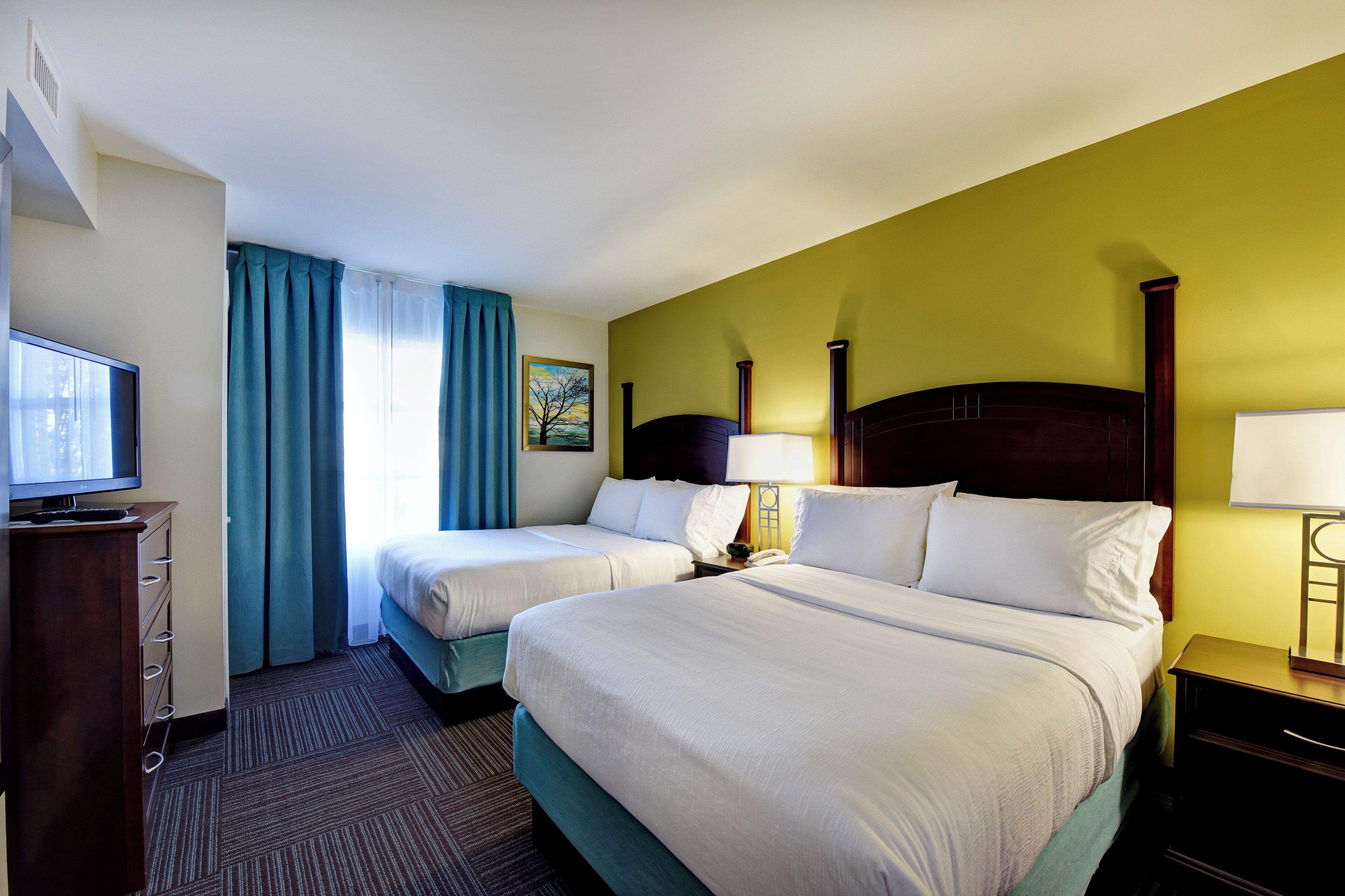 A hotel room with two beds, a television, a desk, and a painting on the wall.