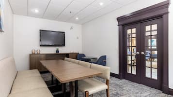 Un salón de conferencias con una larga mesa, un sofá color beige y una televisión montada en la pared.