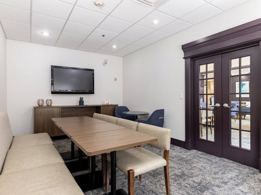 A conference room with a long table, beige sofa, and a TV mounted on the wall.