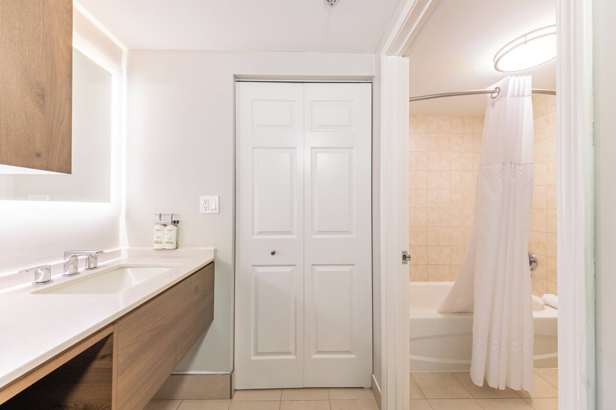 A bathroom with a white sink, wooden vanity, a white door, and a shower with a white curtain.