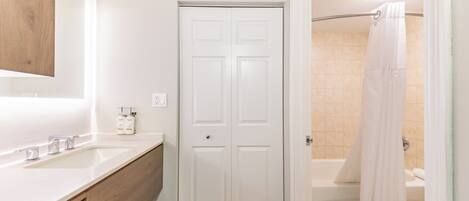 Un baño con tocador blanco, una puerta y una zona de ducha.