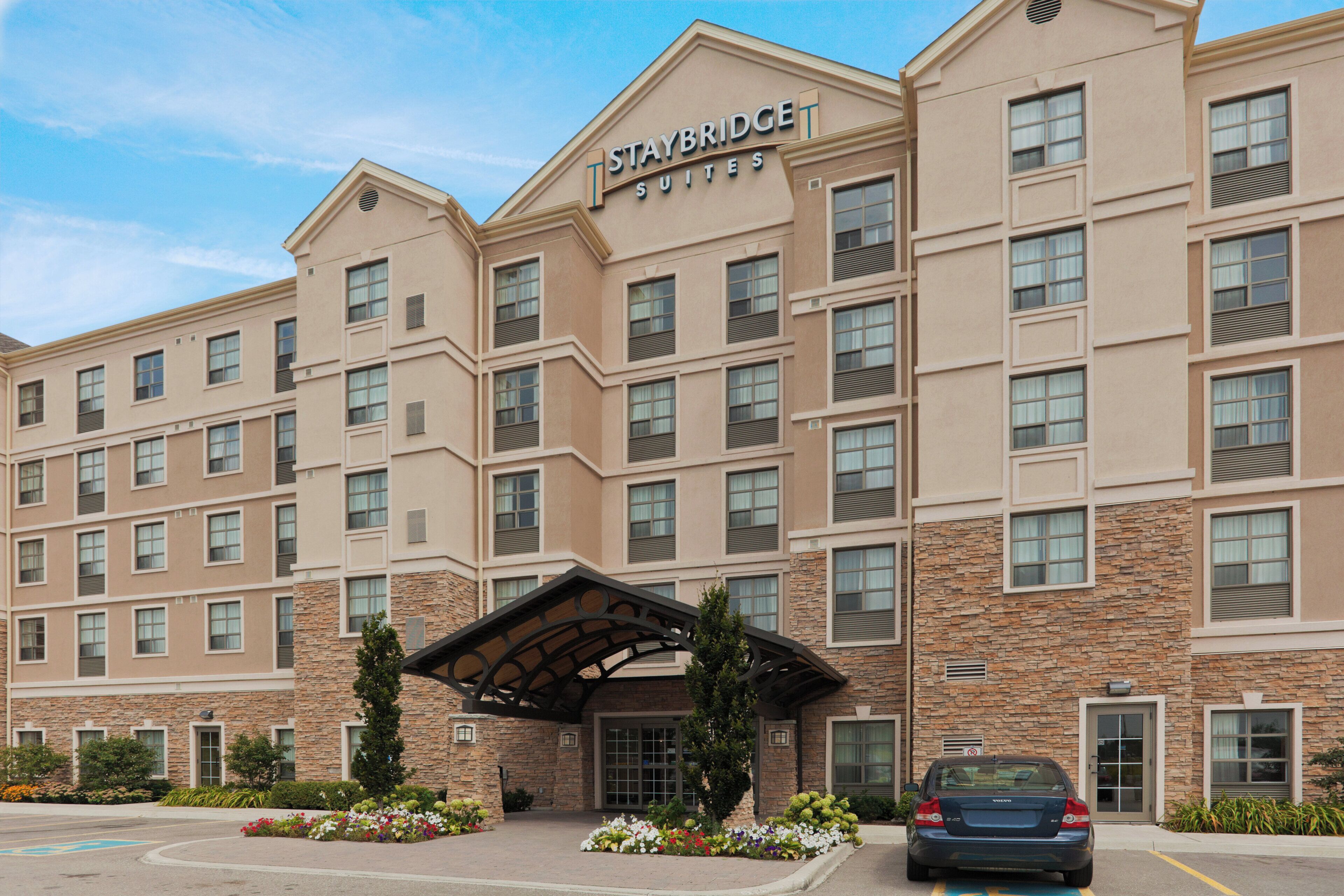 Un hotel Staybridge Suites con fachada de piedra, múltiples ventanas y un acceso cubierto.