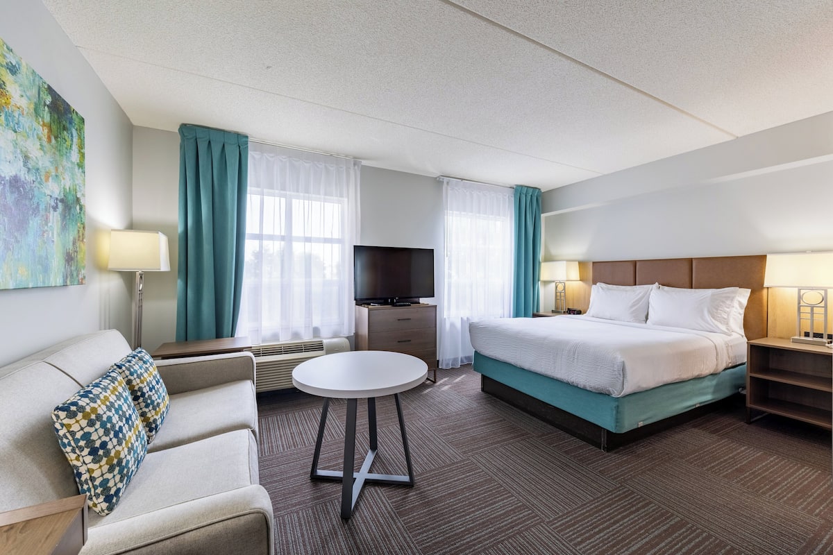 A hotel room with a bed, a sofa, a TV, a desk, and a lamp.