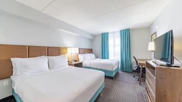 Una habitación de hotel con dos camas, un escritorio con computadora, televisión y lámpara.