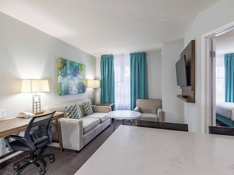 A hotel room with a desk, two sofas, a TV, and a bed.