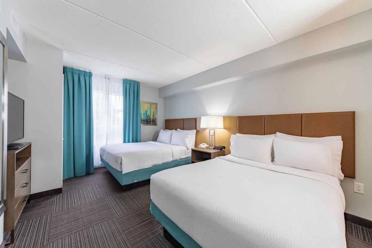 A hotel room with two beds, a TV, a desk with drawers, a lamp, and a painting on the wall.