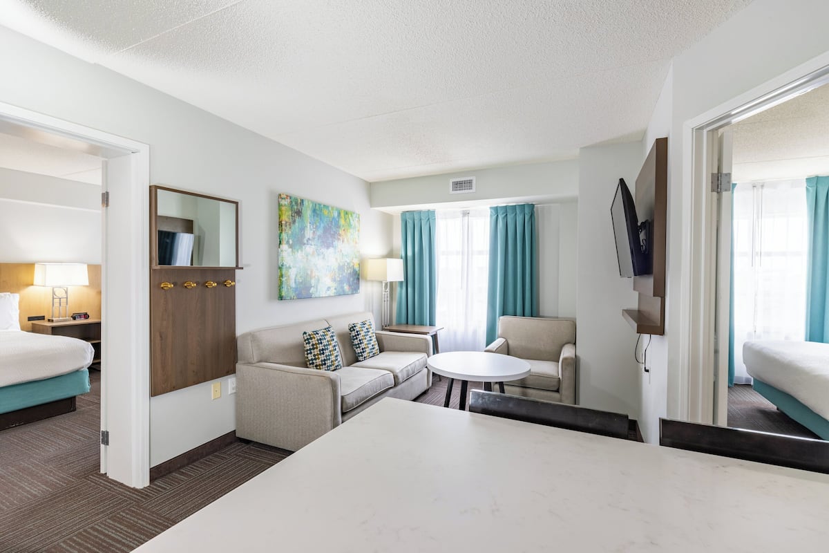 A hotel room with a bed, a sofa, a small table, a chair, a desk, and a window with curtains.