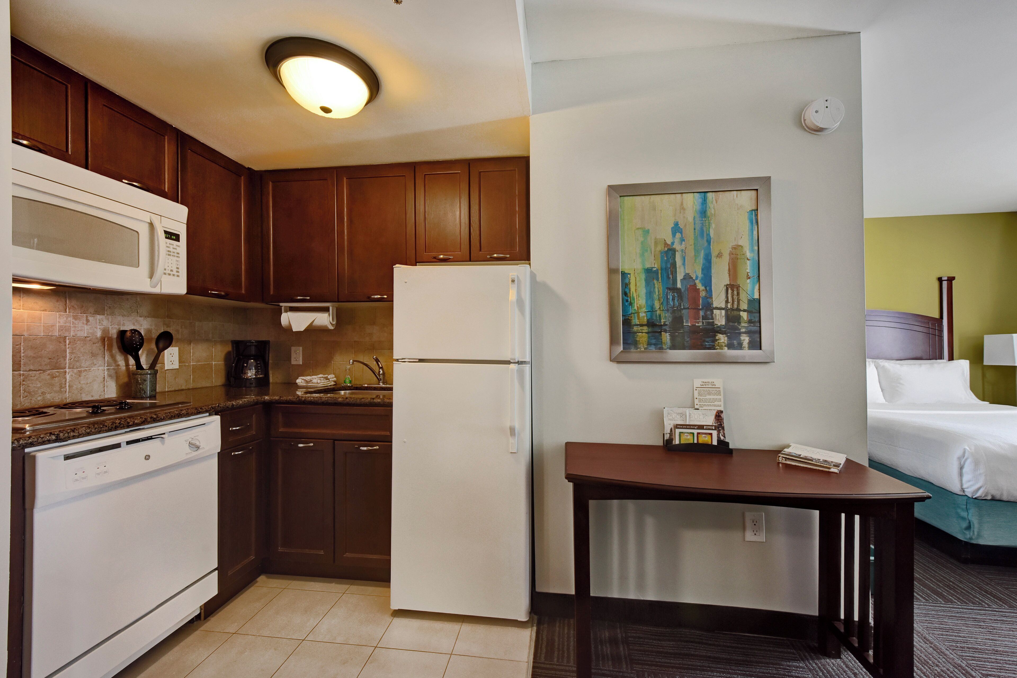 Una habitación de hotel compacta con kitchenette, una cama y un cuadro en la pared.