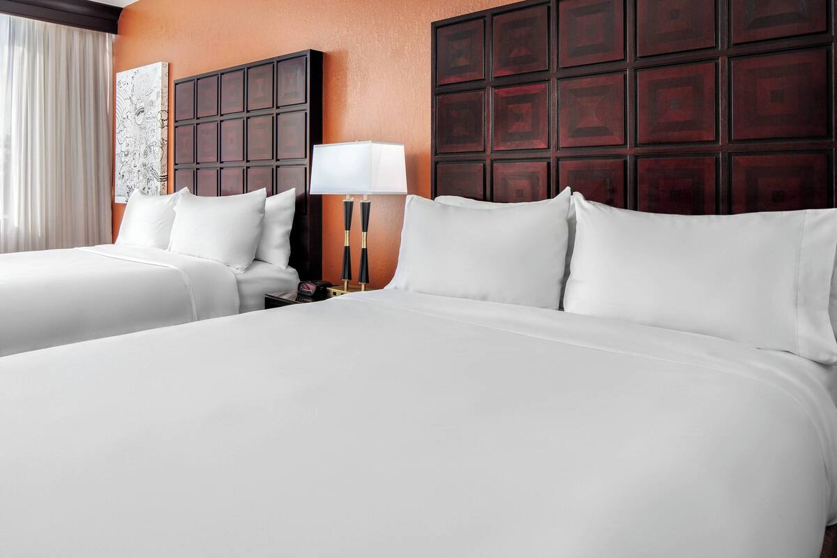 A hotel room with two beds, a nightstand, a lamp, and a large artwork on the wall.