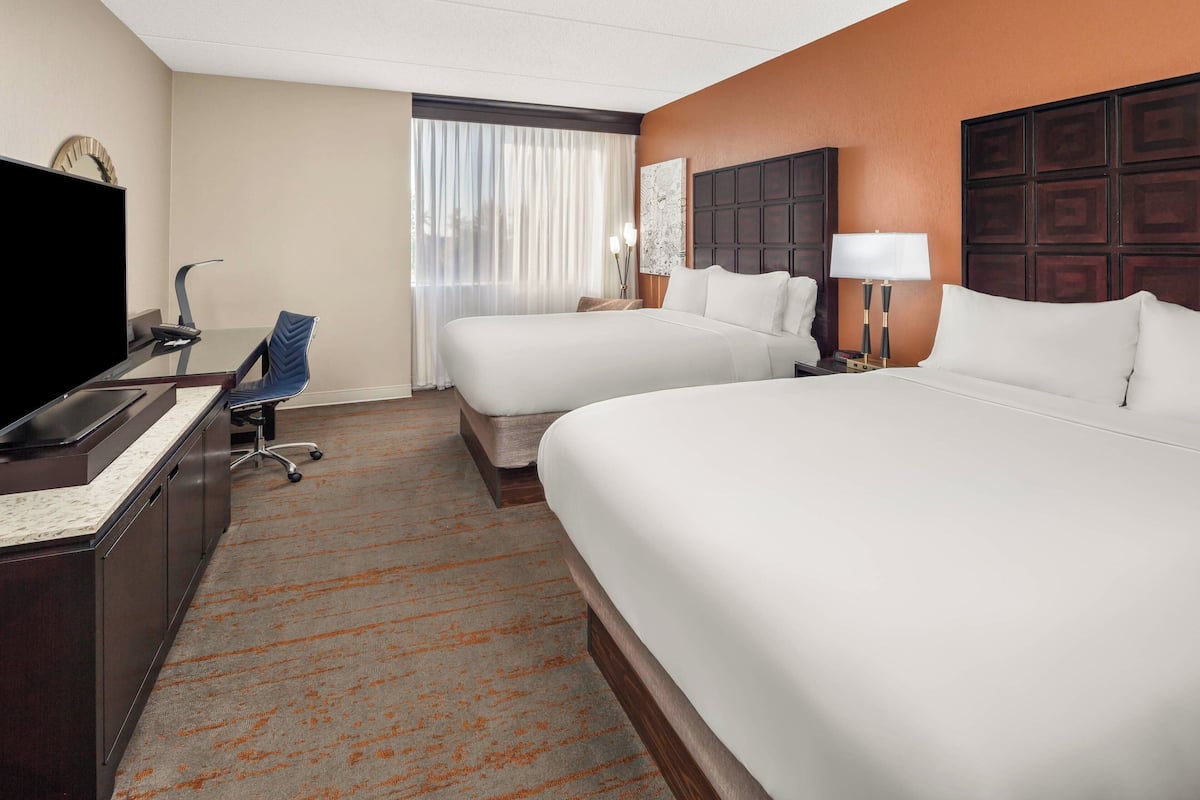 A hotel room with two beds, a desk with a television, a chair, and a window with curtains.