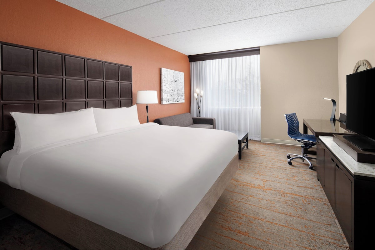 A hotel room with a large bed, a desk with a computer, a chair, and a television.