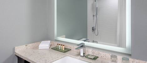 Un baño moderno con lavamanos de mármol, un espejo grande y una cabina de ducha de vidrio.