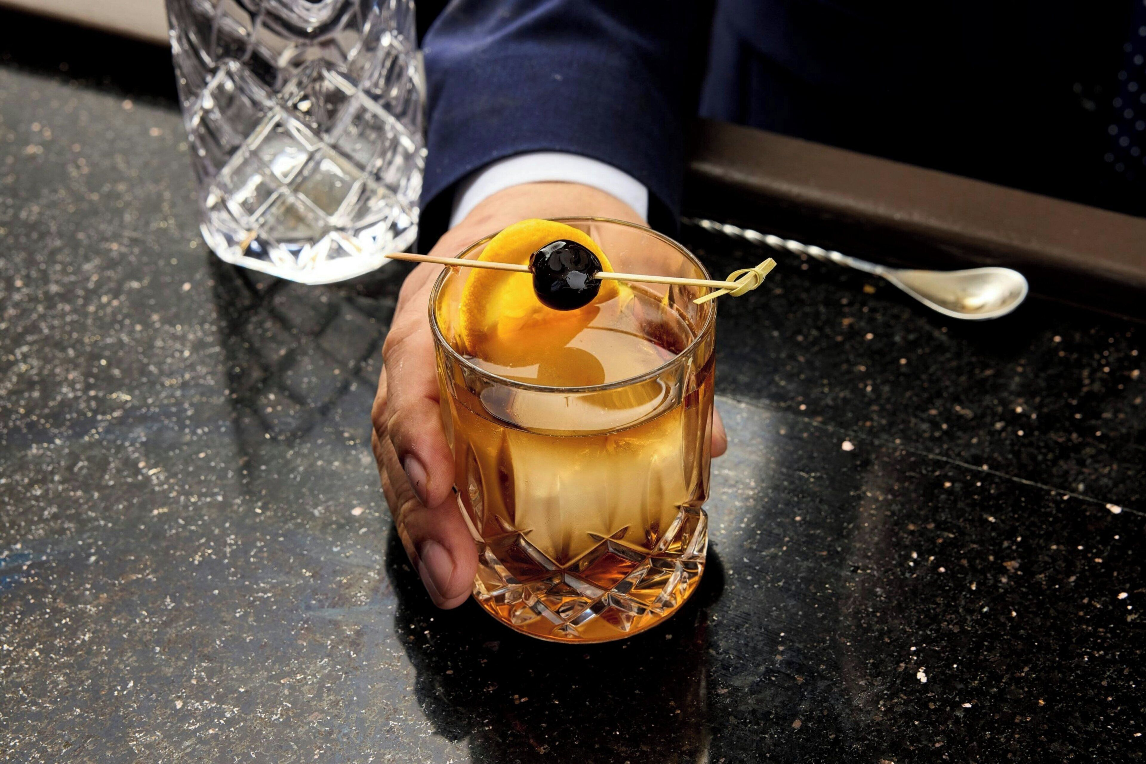 A hand holding a glass with a cocktail garnish.